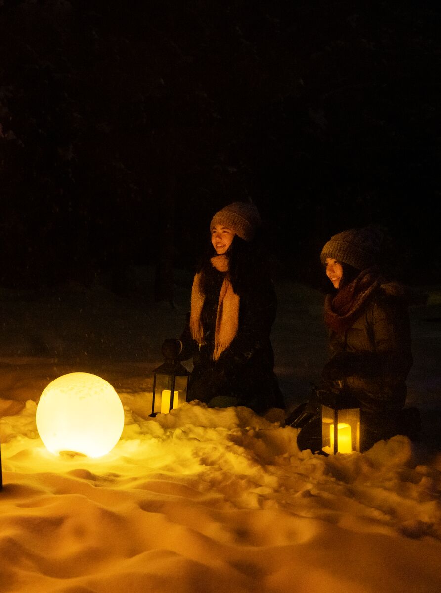Two girls sit in front of a light-up polar bear at In Search of Christmas Spirit in Banff National Park.
